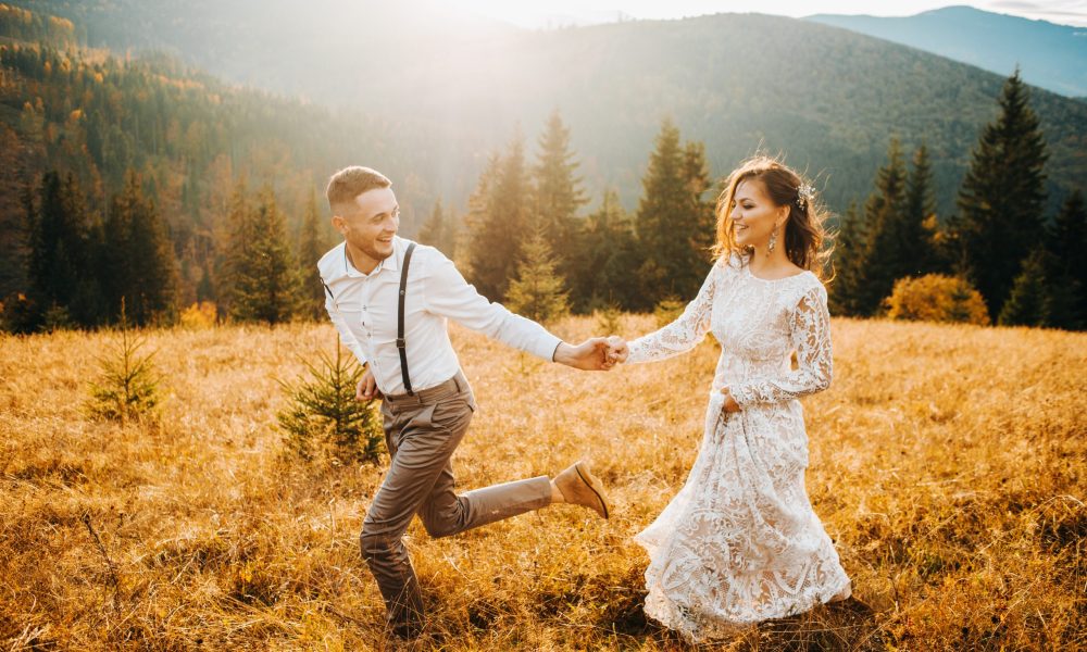 Photographie d'un couple de mariés heureux courant dans un champ, symbolisant l'union et le choix d'alliances L'Alliancier.